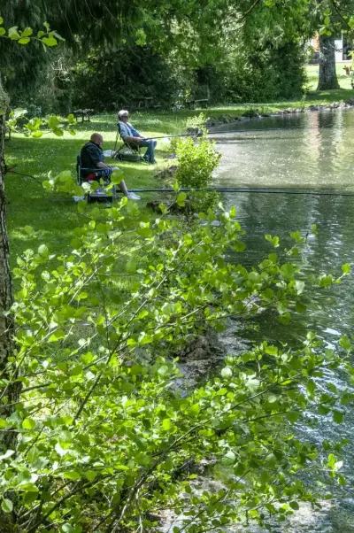 Pêcheur au bord d'un étang ombragé du camping Les Étangs de Plessac