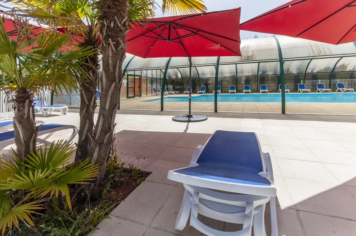 Solarium extérieur avec parasols et vue sur la piscine couverte
